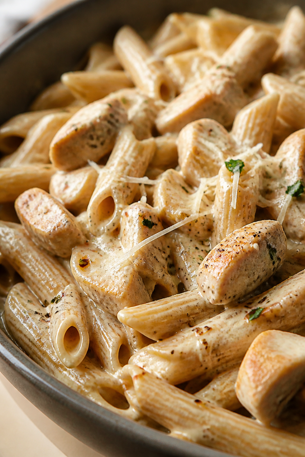 Close-up detail: Creamy chicken Alfredo-coated whole-wheat penne fresh from the skillet, showing ten