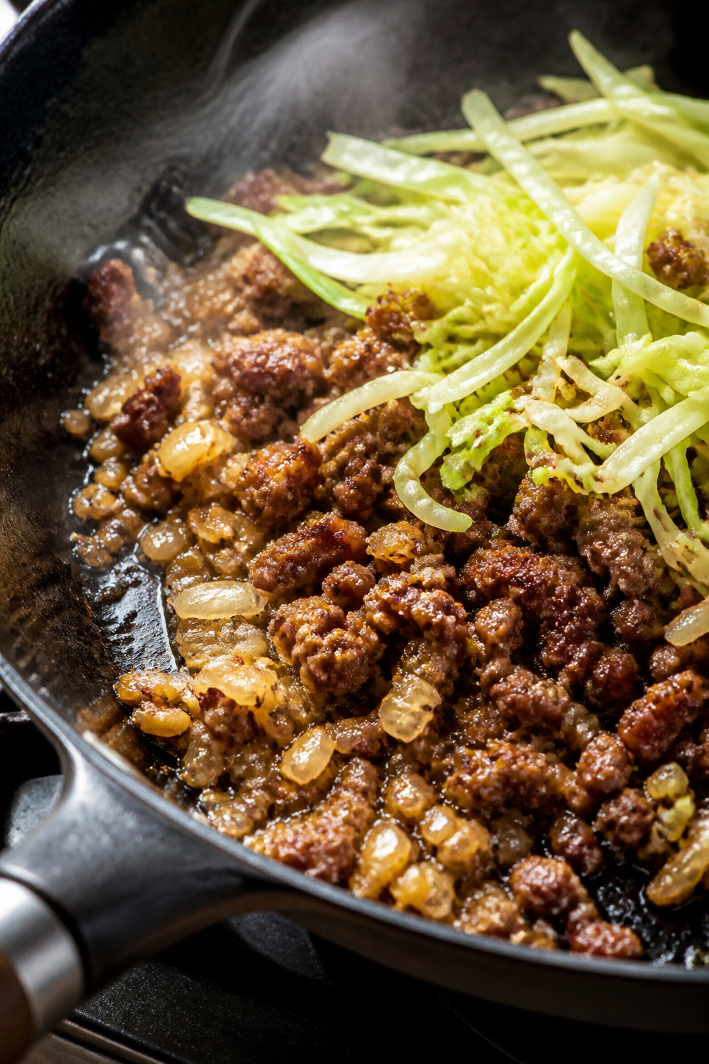 Cooking process, close-up: Sizzling ground beef browning in a wide, black skillet over medium-high h