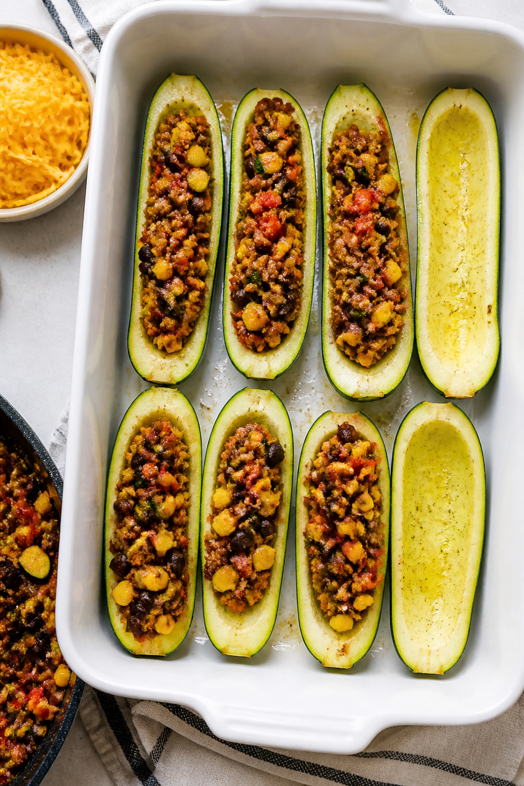 Cooking process: Overhead shot of par-baked zucchini halves being filled with thick, well-seasoned t