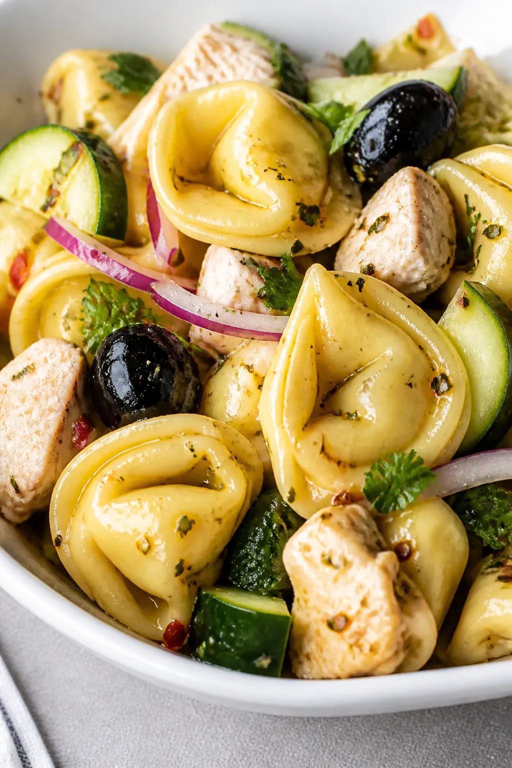 Close-up detail: Al dente cheese tortellini tossed with diced rotisserie chicken, glossy black olive