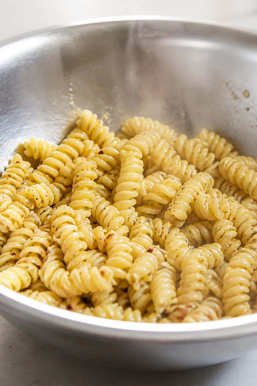 Cooking process close-up: Al dente rotini just drained and lightly rinsed, steam rising, beads of wa