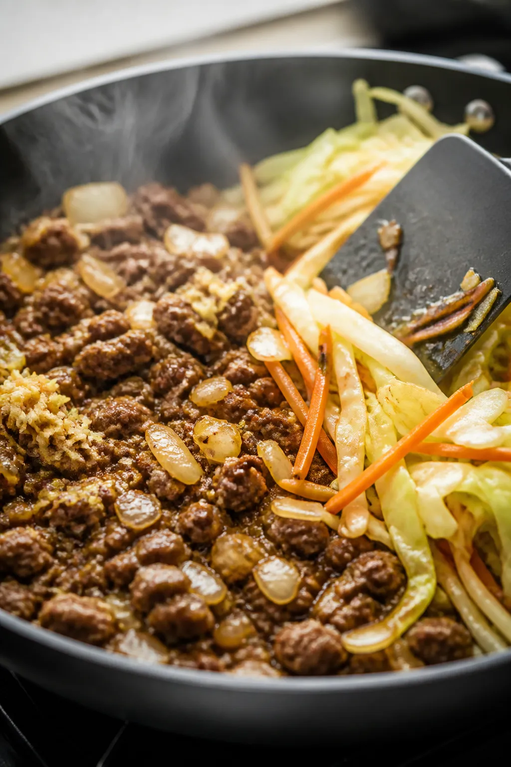 Cooking process, close-up detail: Sizzling skillet of browned lean ground beef with sautéed diced y