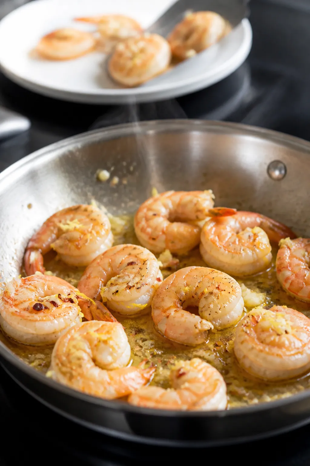 Cooking process, close-up: Medium-close shot of shrimp sizzling in a stainless steel skillet, just-o