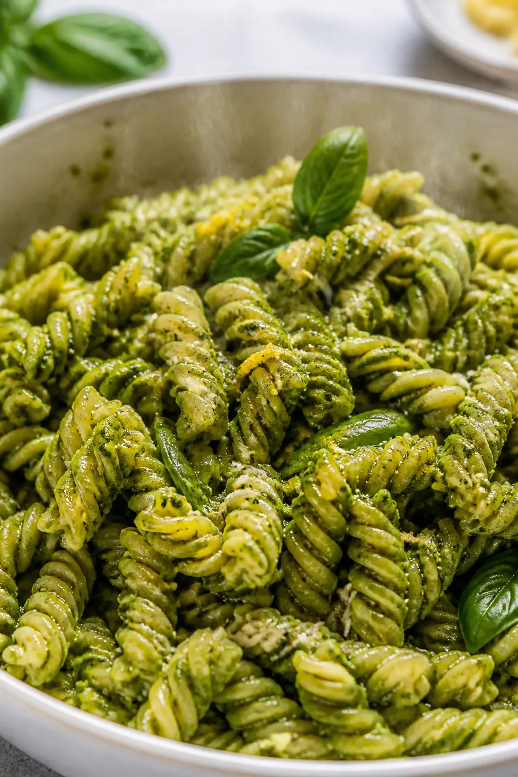 Cooking process close-up: Slightly warm al dente fusilli being tossed in a large bowl with glossy ba