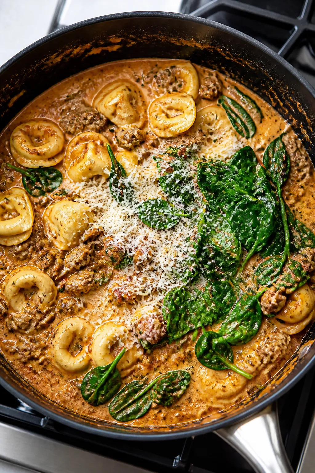 Cooking process: One-pan creamy beef and spinach tortellini mid-simmer in a deep, black skillet—to