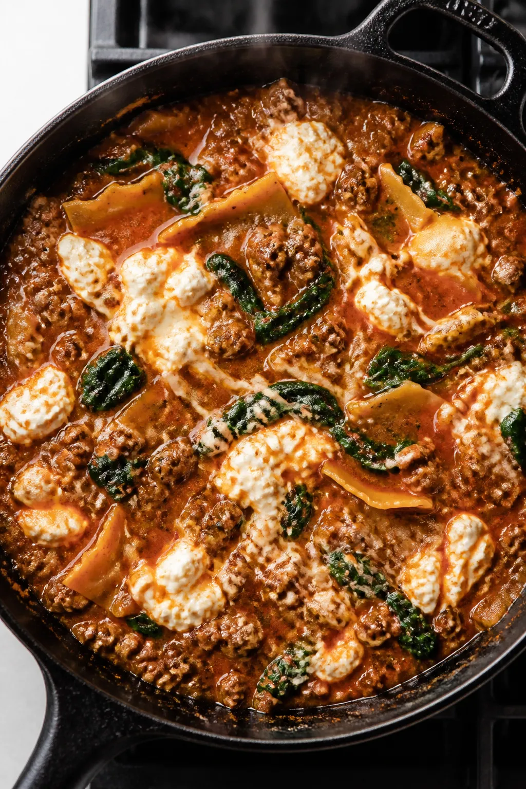 Cooking process, overhead skillet: Overhead shot of the hamburger lasagna skillet mid-simmer, showin