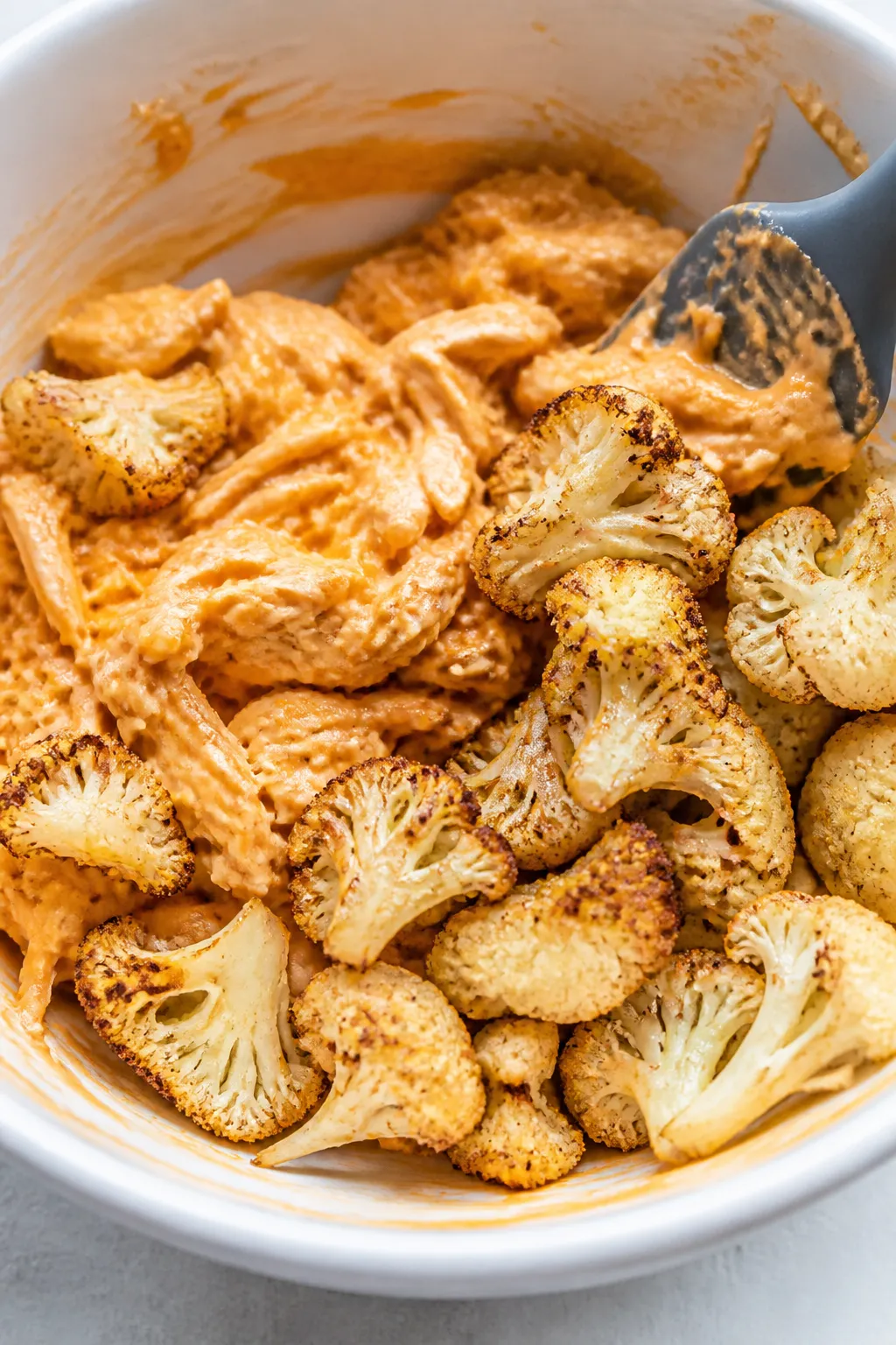 Cooking process shot: the roasted cauliflower being folded into the creamy buffalo mixture in a larg