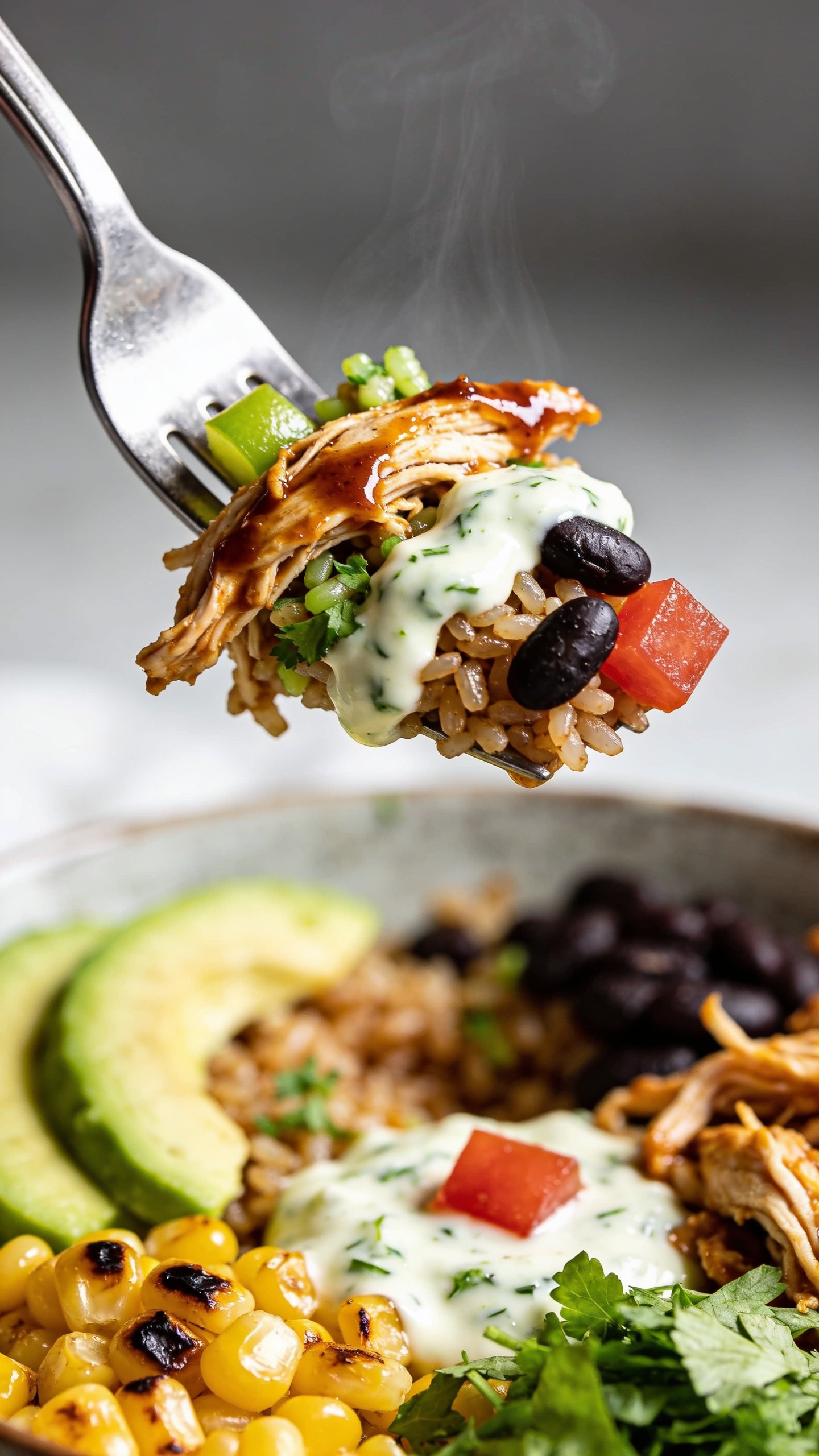 Action close-up capturing the single most irresistible bite: a stainless fork lifting the perfect mouthful from the same burrito bowl, one second before the bite reaches the mouth. The fork holds shredded rotisserie chicken coated in glossy chipotle-lime sauce, a few grains of cilantro-lime brown rice clinging, a swipe of creamy yogurt-cilantro crema, a black bean or two, and a tiny cube of tomato, with steam subtly visible rising. The bowl remains beneath, slightly blurred but clearly showing avocado slices, charred corn, and cilantro. Bright natural side light, shallow depth of field with tack-sharp focus on the lifted bite and glistening sauce; no hands visible, only the utensil tip entering the frame. Food fills 90–95% of the image, movement and anticipation emphasized.