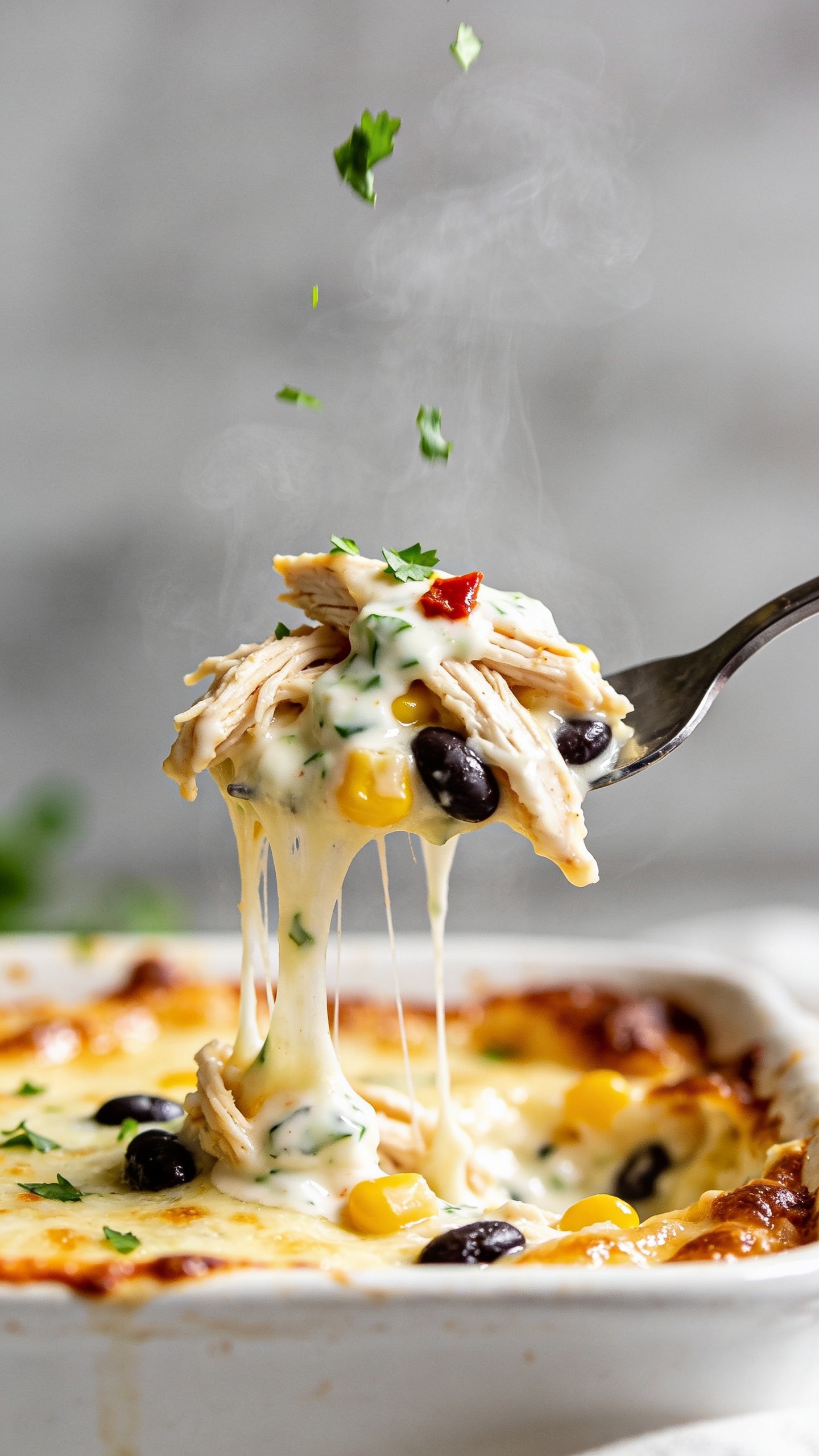 Dynamic action close-up capturing a fork lifting the perfect gooey bite from the same casserole, one second before it reaches the mouth. The lifted bite shows stretchy melted cheese pulling long strands from the pan, with visible rotisserie chicken shreds, a few black beans, corn, and a fleck of red pepper all coated in the creamy yogurt-salsa sauce. No hands, only the fork tip in frame. Steam rising, tiny cilantro confetti falling midair onto the bite, glistening edges and browned cheese crust in the background bokeh. Bright natural lighting, shallow depth of field, food filling 90–95% of the frame for irresistible movement and texture.
