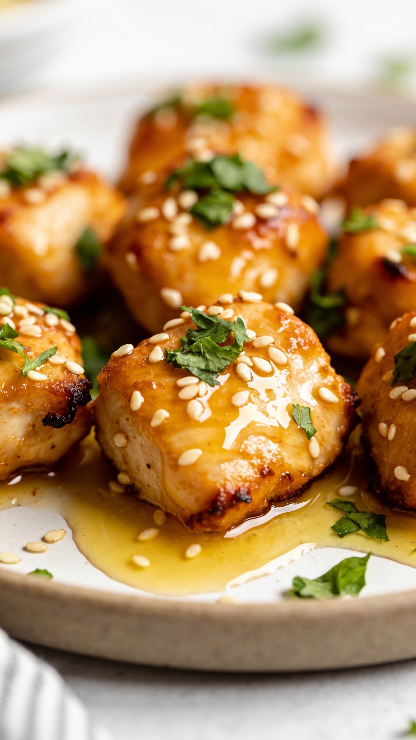 A stunning hero shot of the finished High Protein Air Fryer Garlic Butter Chicken Bites plated perfectly, glossy golden-brown crust on bite-sized pieces, bright garlic butter glaze pooling slightly, crispy edges visible, fresh parsley and sesame seeds dusted, vibrant plate styling, natural light, shallow depth of field, no people or hands in frame.