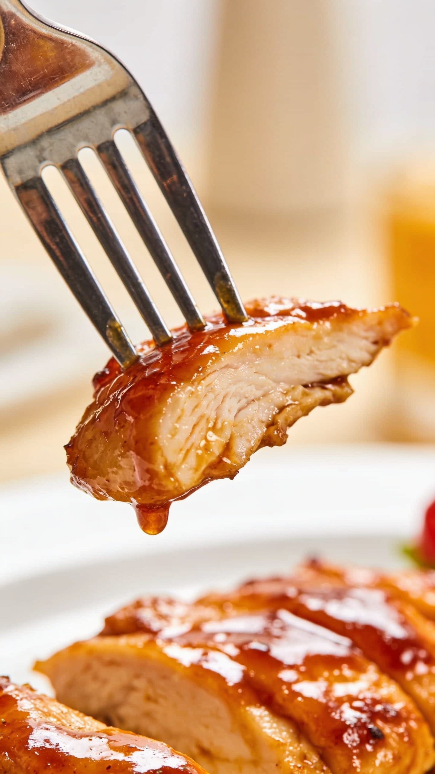 A close-up, dynamic action shot: a fork is impaling a perfect bite of the finished chicken, lifting it slightly away from the plate as glossy sauce clings to the meat. The frame captures the moment just before the bite, with a shallow depth of field keeping the bite in sharp focus and the background softly blurred to emphasize texture and shine of the glaze.