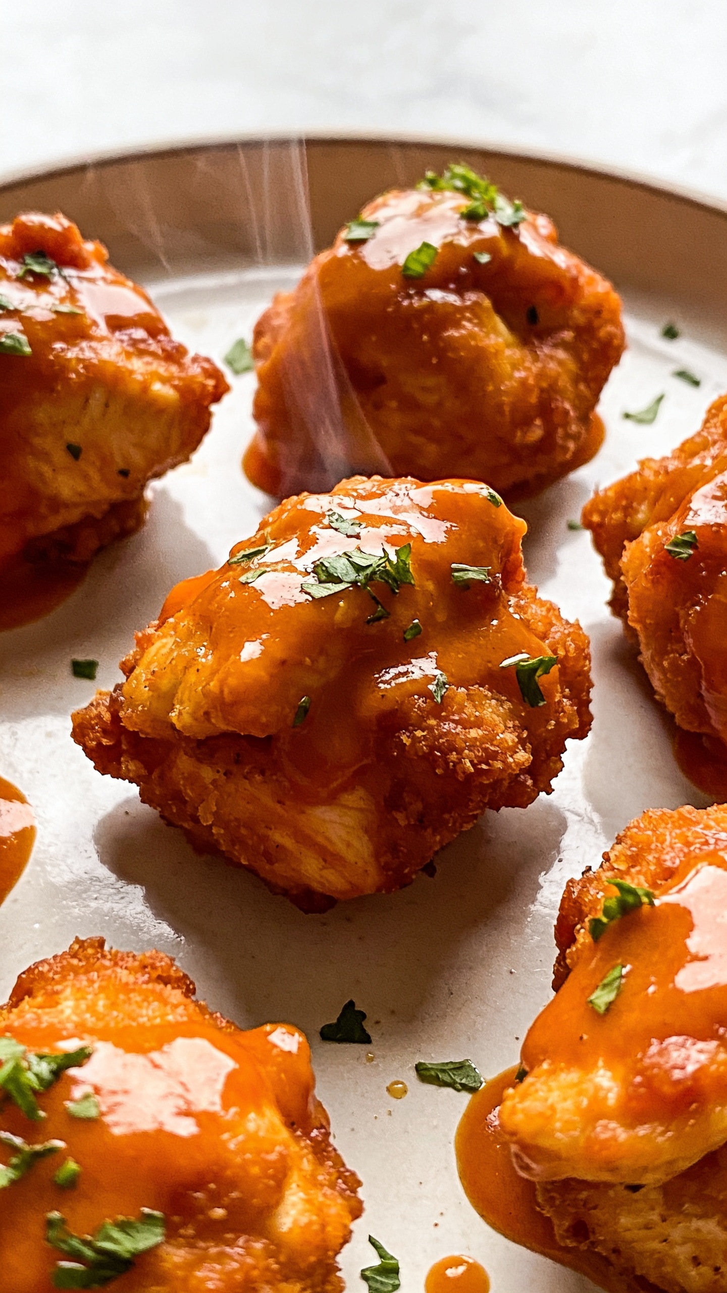 Close-up, high-detail stills of the finished dish from a different angle: a top-down view of several buffalo chicken bites arranged on the plate, highlighting crispy coating, creamy interior (hint of yogurt-based sauce visible), steam subtly rising, and fresh chopped herbs lightly dusted over the top. Ultra-close, 90–95% food, bright natural light, glossy shine on sauce, rich textures, premium food-blog styling; no utensils, hands, or people.