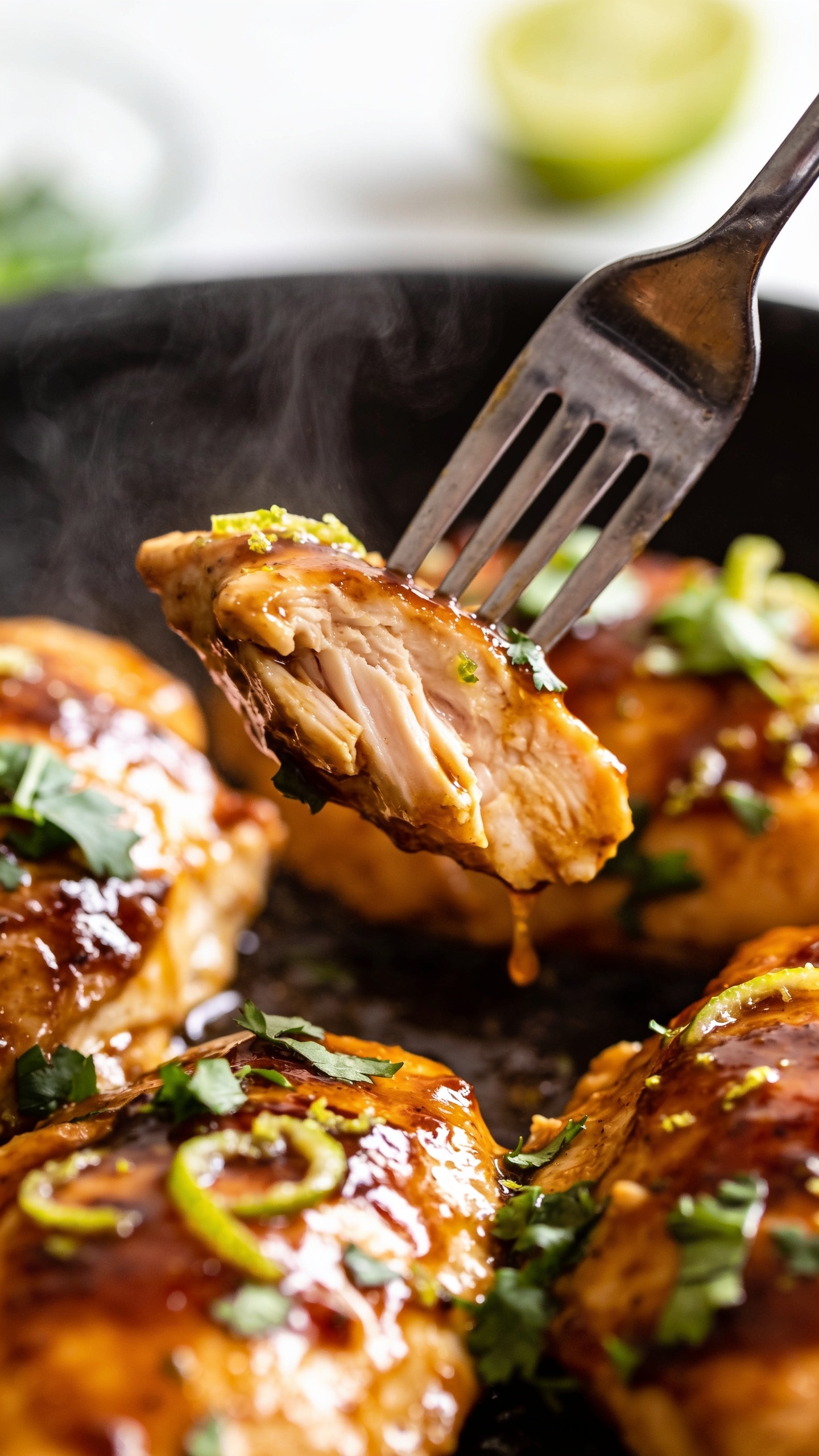 A dynamic close-up action shot capturing the moment a fork lifts the perfect bite of the finished dish. The fork is angled to scoop a piece of juicy chicken with a glossy sauce clinging to the surface, steam just beginning to rise, cilantro flecks and lime zest catching the light. The background is softly blurred, the food filling 90–95% of the frame, natural bright lighting, premium food-blog styling, no hands visible.