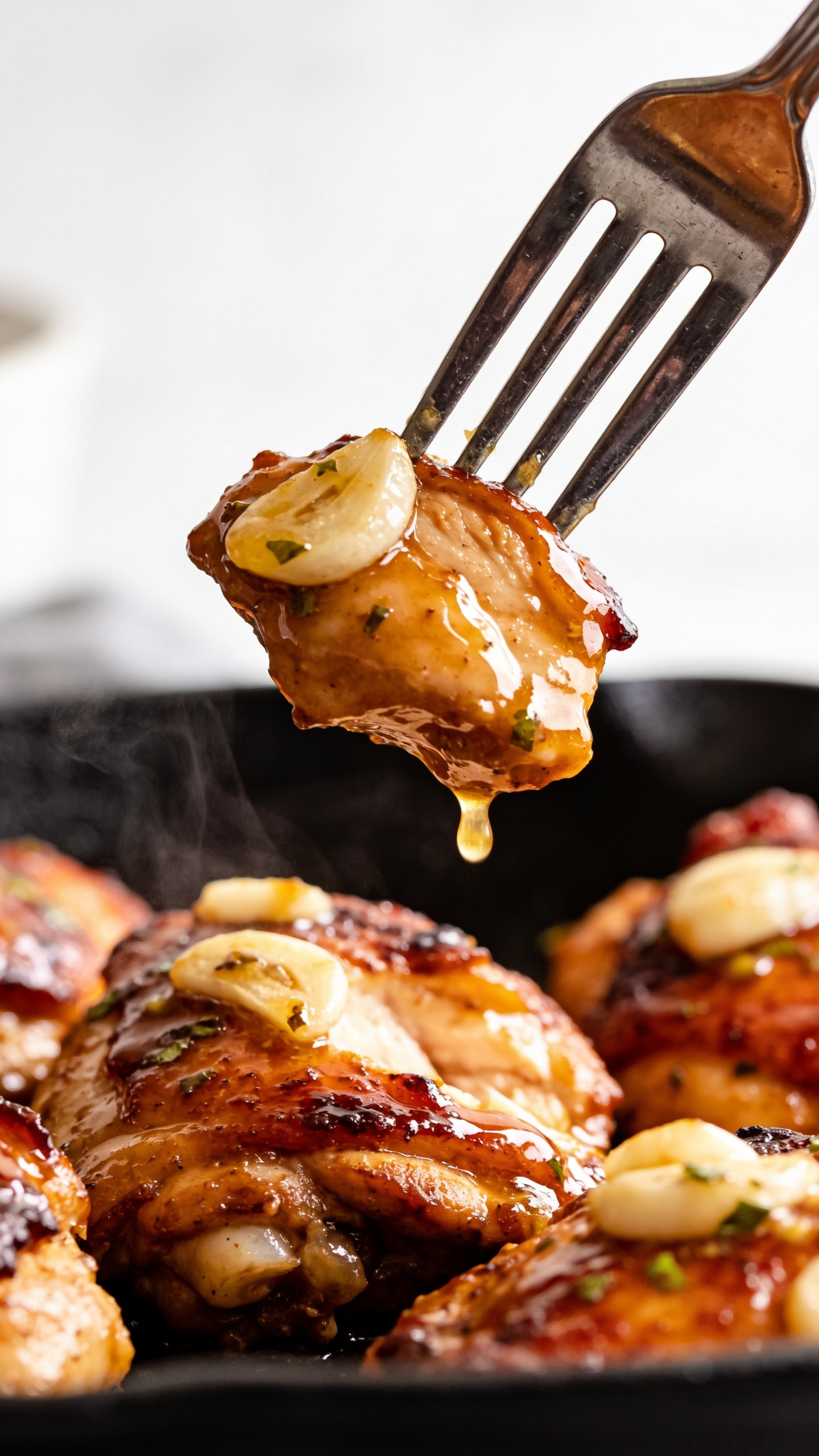 A dynamic close-up action scene: a fork lifting the perfect bite of juicy garlic butter chicken thigh, the glossy sauce clinging to the fork, steam subtly rising, vibrant colors and textures emphasized, shallow depth of field, bright natural lighting, food dominating frame, no hands or faces.