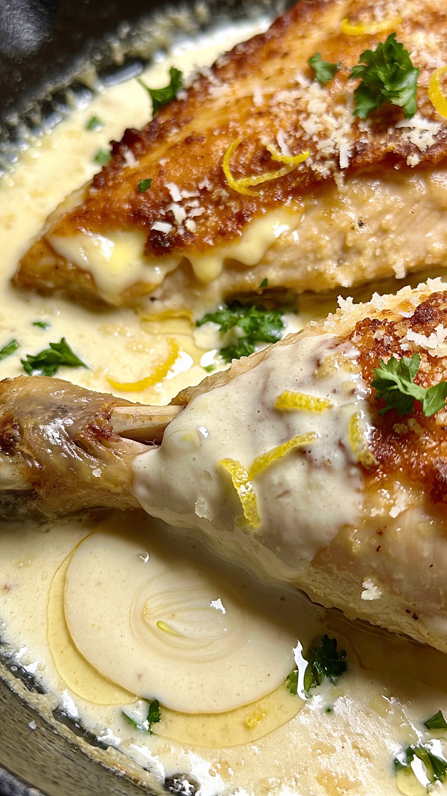Close-up multi-angle view of the finished dish emphasizing texture: a top-down shot showing the creamy coating on the chicken, the crispy skin, and melted parmesan around the edges. A second shallow-angle detail focuses on the garlic cream pooling beside the thigh, with fresh parsley and lemon zest micro-garnish adding vibrant color. Lighting is bright and natural, highlighting depth, moisture, and the luxurious sauce.