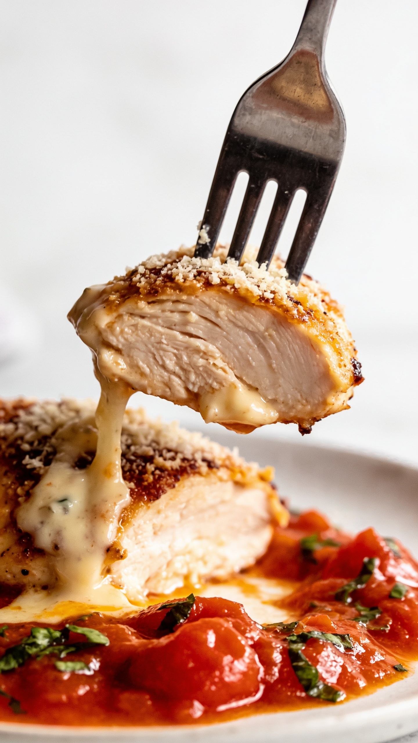 A dynamic close-up of a fork about to take the perfect bite: a juicy chicken thigh lifted slightly from the plate, showcasing melted parmesan crust, creamy sauce coating, and a glistening tomato-herb sauce underneath; the fork is the only utensil visible, no hands, shallow depth of field, vibrant colors, studio-quality food photo look, 3:2 aspect.